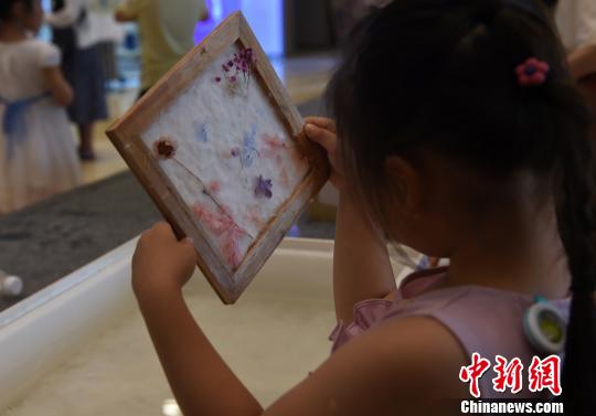 图为小朋友欣赏自己制作的古法花草纸。　周毅 摄